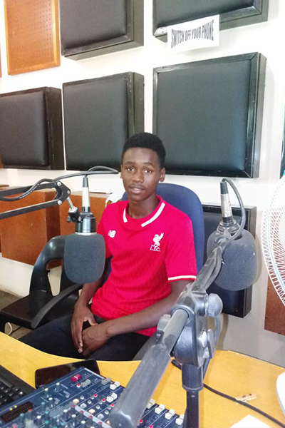 A young man wearing a red T-shirt is sitting behind a microphone.